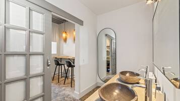 Un baño moderno con dos lavamanos de piedra grandes, un espejo amplio y una puerta que da a un comedor con taburetes de bar.
