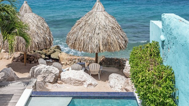 A poolside area with a view of the ocean, thatched umbrellas, and white chairs. - PM78 Boutique Apartments (Willemstad)