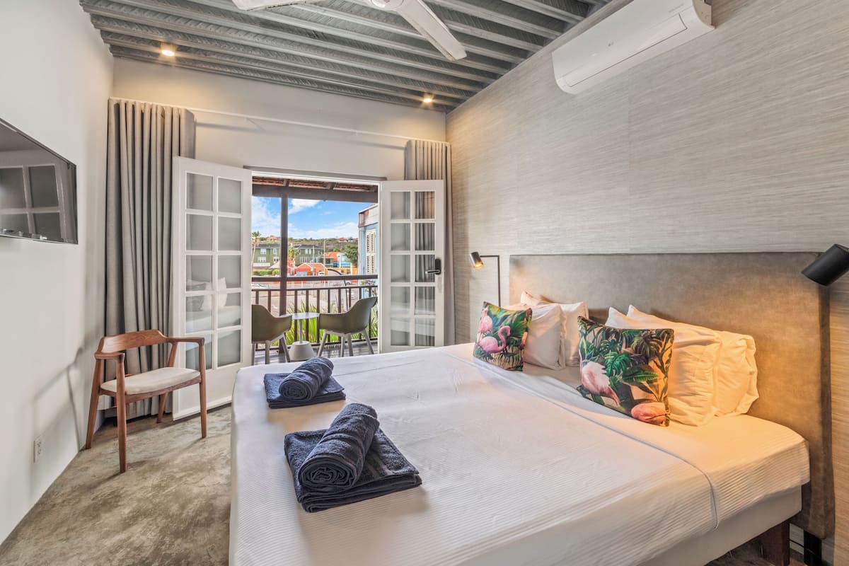 Ein Hotelzimmer mit einem großen Bett, einem Sessel, einem Balkon mit Aussicht und einem Deckenventilator.