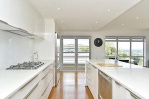 Uma cozinha moderna com fogão a gás, armários brancos e vista para o exterior através de amplas portas deslizantes.