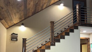 Una escalera de madera con barandilla metálica, una mesa de madera y un cartel en la pared que dice 'Welcome to the Lake House'.