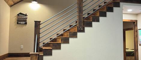 A wooden staircase with a metal railing, a wooden table, and a 'Welcome to the Lake House' sign on the wall.
