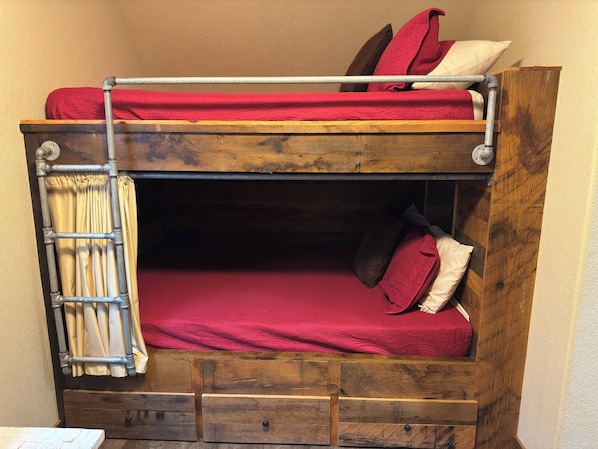 A bunk bed with a metal ladder, a wooden lower bunk, and a red bedspread.