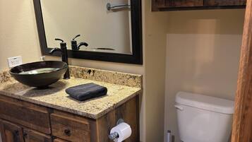 A bathroom with a wooden vanity, a large mirror, a vessel sink, a toilet, and a patterned rug.
