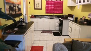 Una cocina compacta con armarios blancos, una estufa y un lavamanos. Hay una cortina roja y un cuadro en la pared.