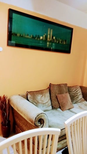 Una sala de estar con un sofá, dos almohadas, un cuadro en la pared y una mesita con un jarrón.