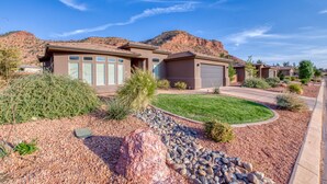 A residential area with modern houses, a well-maintained lawn, and a rocky mountain backdrop.