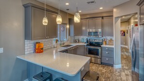 A modern kitchen with a large island, stainless steel appliances, and pendant lighting.