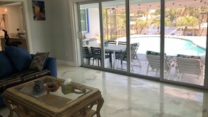 En rummelig stue med en stor skydedør, der fører ud til en udendørs terrasse med en pool.