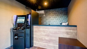A reception area with a coffee machine, a digital screen, and a patterned wall. - Hotel R9 The Yard Oyamakizawa (Oyama)