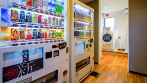Two vending machines with various beverages and snacks, a washing machine, and a wooden floor in a hallway. - Hotel R9 The Yard Oyamakizawa (Oyama)