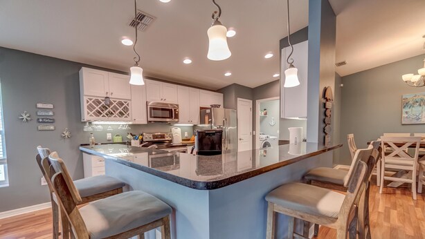 A modern kitchen with a central island, bar stools, and a dining area with a table and chairs. - Located 6 miles from 4 major beaches & walking distance to Shamrock Nature Park (Venice)