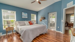 A bedroom with a bed, wooden floor, ceiling fan, and a view of the outdoors through a window. - Located 6 miles from 4 major beaches & walking distance to Shamrock Nature Park (Venice)