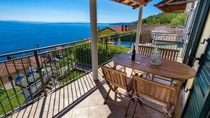 Varanda com mesa e cadeiras, vista para uma piscina e para o mar.