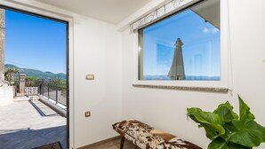 Quarto com um banco, uma planta em vaso e uma janela com vista para uma montanha e céu claro.