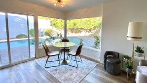 A room with a pool view, a round table with chairs, a rug, and a lamp. - The Litchfield Park Place w/ Heated Pool near Wigwam Golf Resort & State Farm (Litchfield Park)