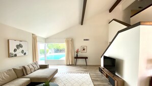 A modern living room with a sofa, a coffee table, a fireplace, and a large window overlooking a swimming pool. - The Litchfield Park Place w/ Heated Pool near Wigwam Golf Resort & State Farm (Litchfield Park)