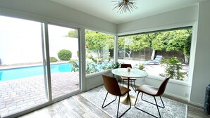 A room with a large sliding glass door leading to a swimming pool, a round table with chairs, and a ceiling light fixture. - The Litchfield Park Place w/ Heated Pool near Wigwam Golf Resort & State Farm (Litchfield Park)
