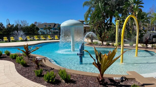 Piscina com uma fonte de água, rodeada por área ajardinada com plantas pequenas e um caminho pavimentado.