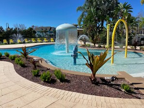 A swimming pool with a water fountain, surrounded by a landscaped area with small plants and a paved walkway.