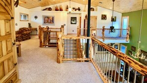 A rustic interior with a wooden staircase, a loft area, and a view of the outdoors. - Majestic Mountain Getaway - Jenson's TreeHouse, a Spacious Cabin Retreat. (Show Low)