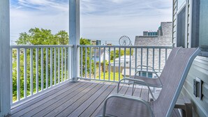 A wooden deck with a white railing, a chair, and a view of a Ferris wheel and buildings in the background. - Park once, walk everywhere. Beach, restaurants, boardwalk & coffee. Easy living. (Carolina Beach)