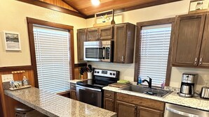 A kitchen with a granite countertop, stainless steel appliances, wooden cabinets, and a bar stool area.