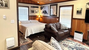A cozy room with a bed, a leather sofa, a patterned rug, and a television.