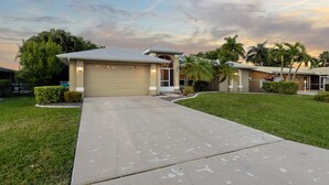 A residential house with a garage, a driveway, and a well-maintained lawn. - Pool Table, Bicycles, Pool & Spa --ESCAPE - Caribbean Getaway - Roelens Vacations (Cape Coral)