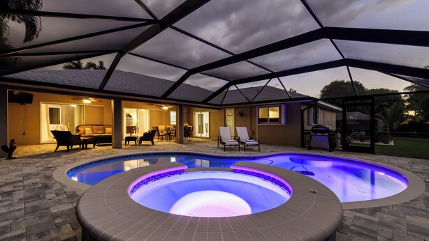 A swimming pool with a hot tub and lounge chairs, surrounded by a covered patio area. - Pool Table, Bicycles, Pool & Spa --ESCAPE - Caribbean Getaway - Roelens Vacations (Cape Coral)