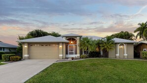 A residential house with a garage, a front porch, and a well-maintained lawn. - Pool Table, Bicycles, Pool & Spa --ESCAPE - Caribbean Getaway - Roelens Vacations (Cape Coral)
