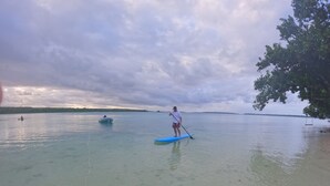 A person standing on a paddleboard in a calm body of water with a cloudy sky in the background. - Absolute Beachfront  villa with private beach (Luganville)
