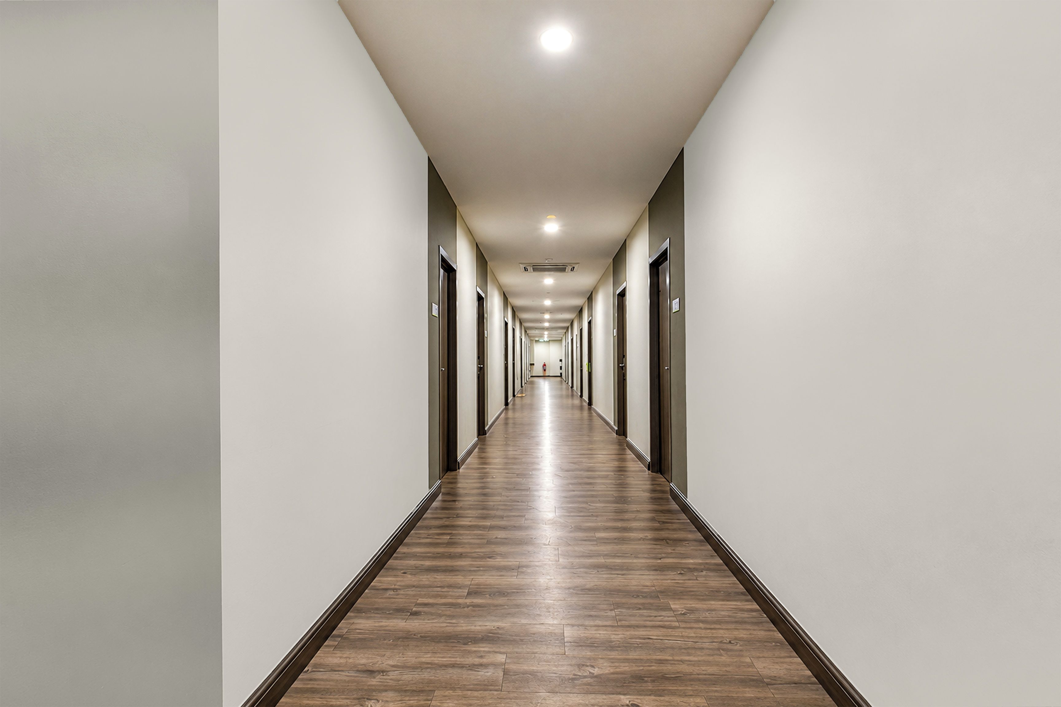 A long, narrow hotel corridor with wooden flooring and doors on both sides.