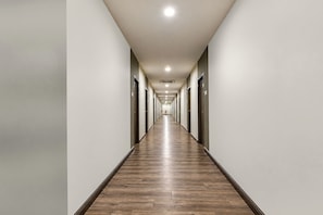 Un long couloir étroit, typique d’un hôtel, avec un plancher en bois et des portes des deux côtés.