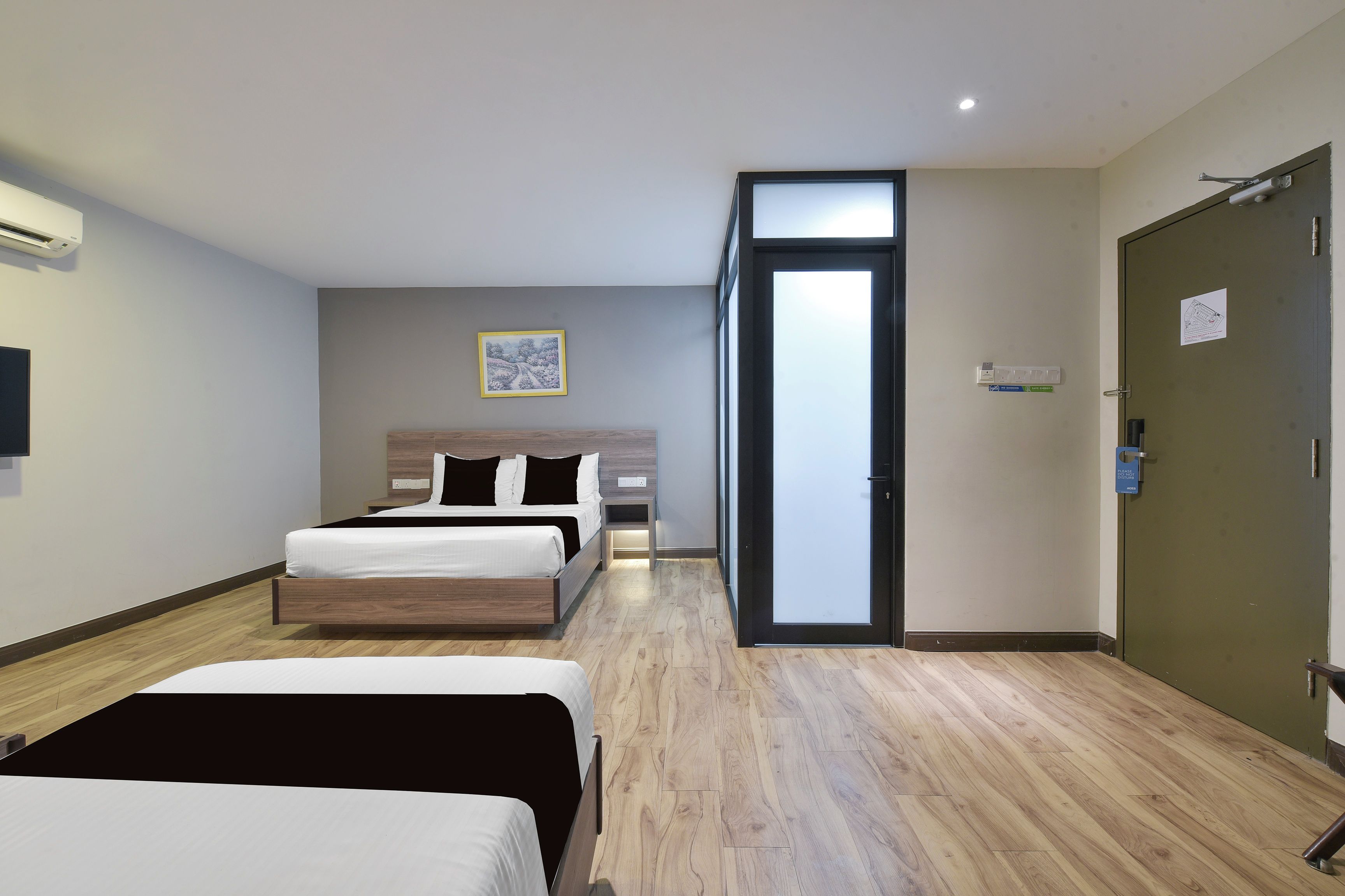 A hotel room with a bed, a bedside table, a wall-mounted TV, and a door leading to another room.