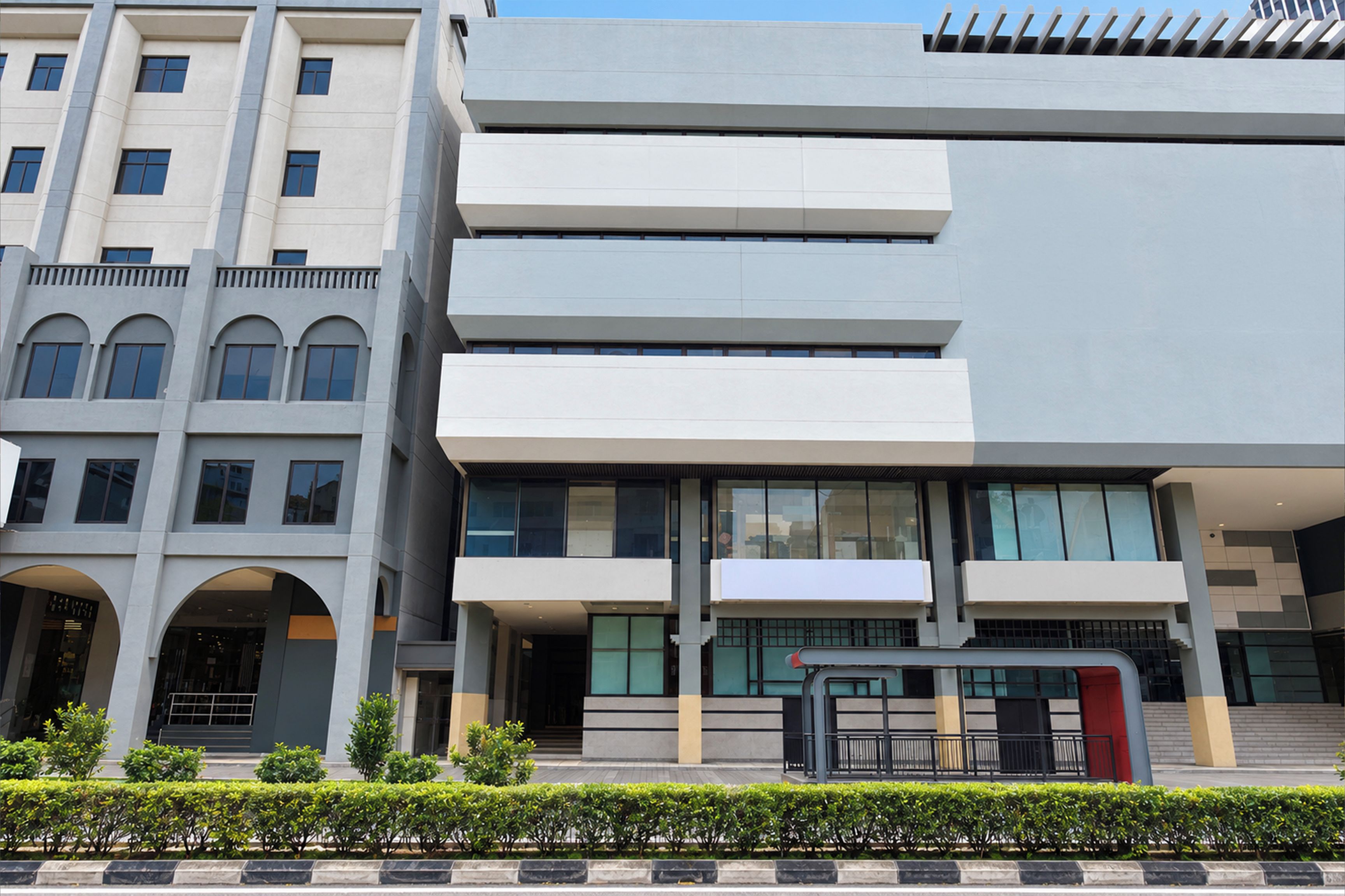 A multi-story building with a modern architectural design, featuring a mix of rectangular and arched windows, a prominent entrance with a glass door, and a flat roof with a series of vertical elements.
