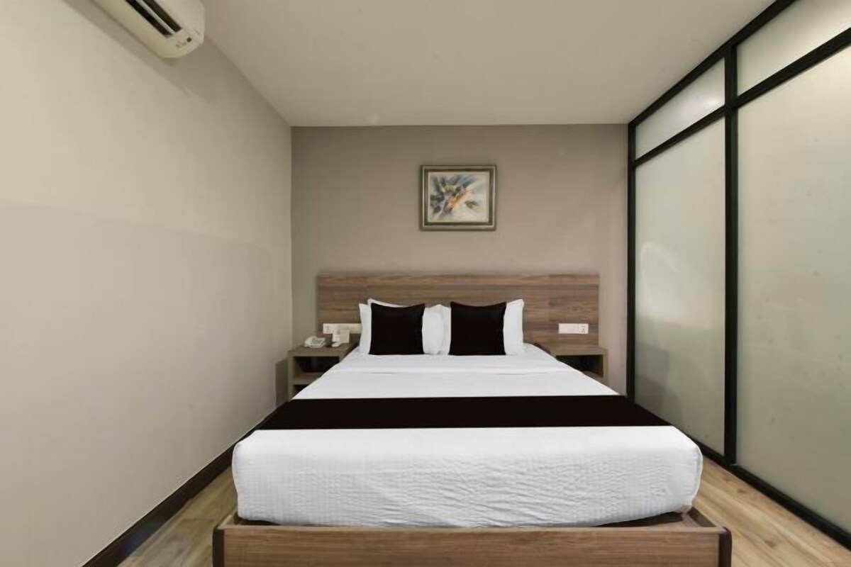 A modern hotel room with a large bed, a wooden headboard, a nightstand, and a wall-mounted air conditioning unit.