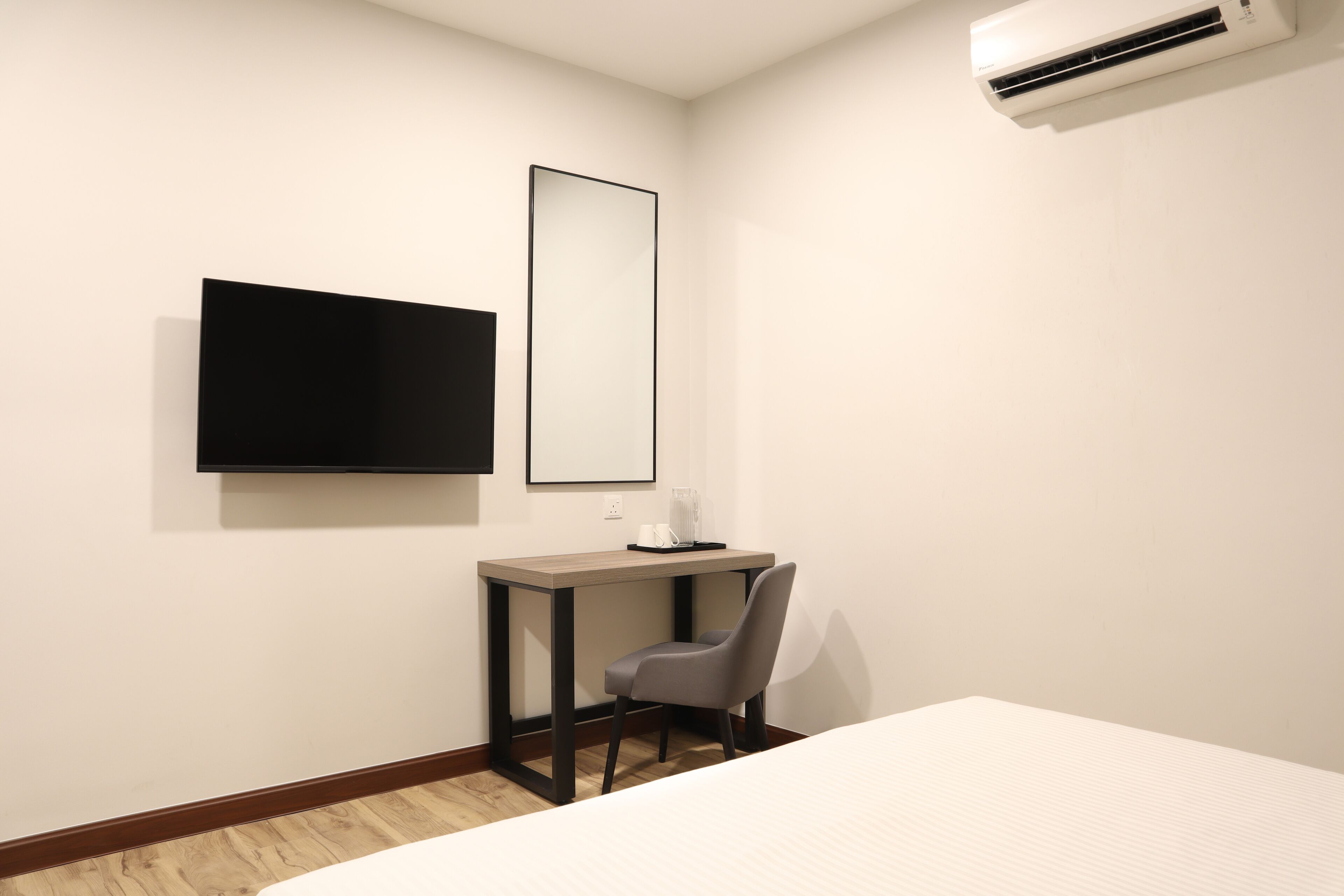 A hotel room with a bed, a desk with a chair, a flat-screen TV, and an air conditioner.