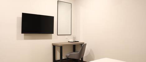 A hotel room with a bed, a desk with a chair, a flat-screen TV, and an air conditioner.