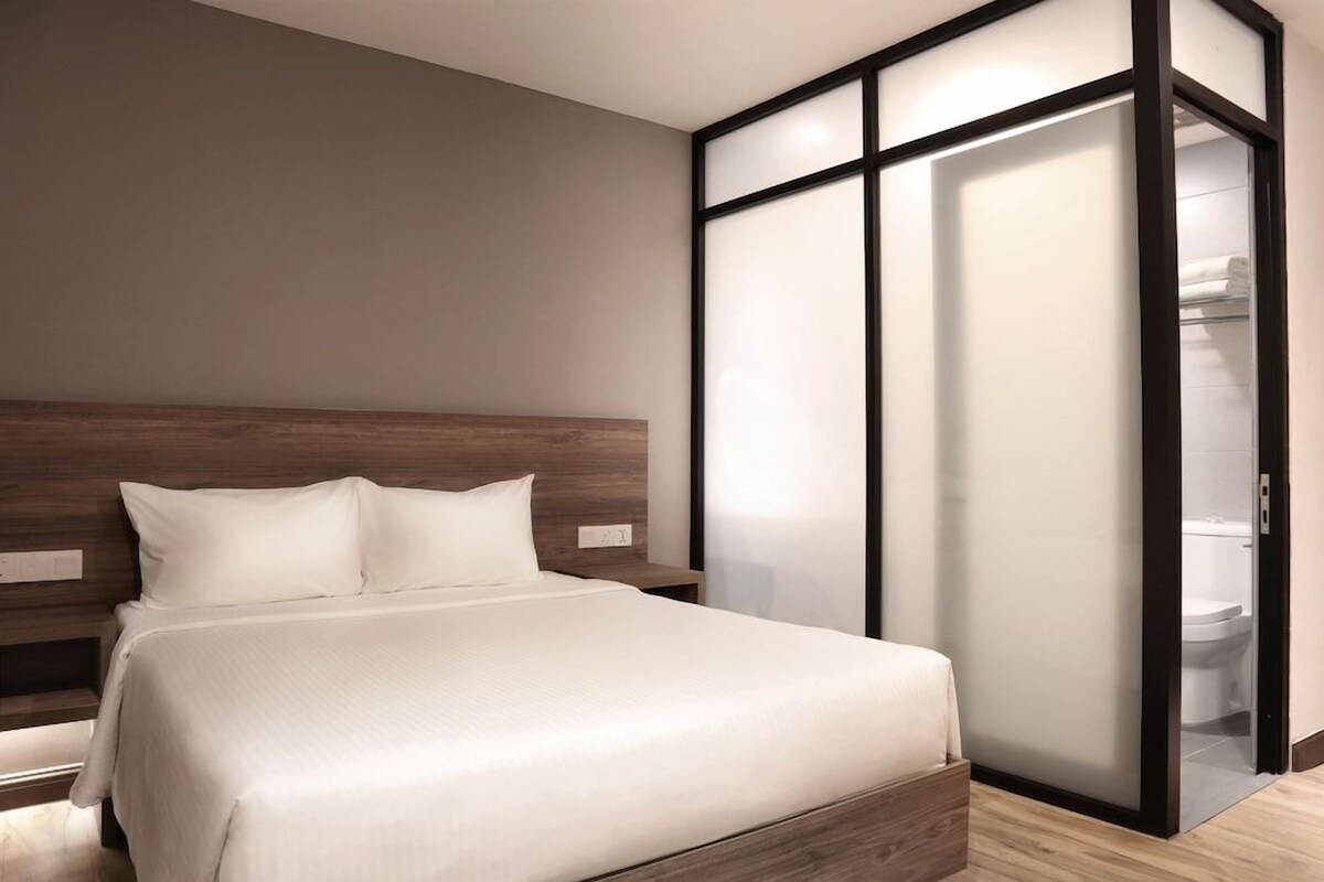 A modern bedroom with a large bed, a wooden headboard, and a frosted sliding door leading to a bathroom.