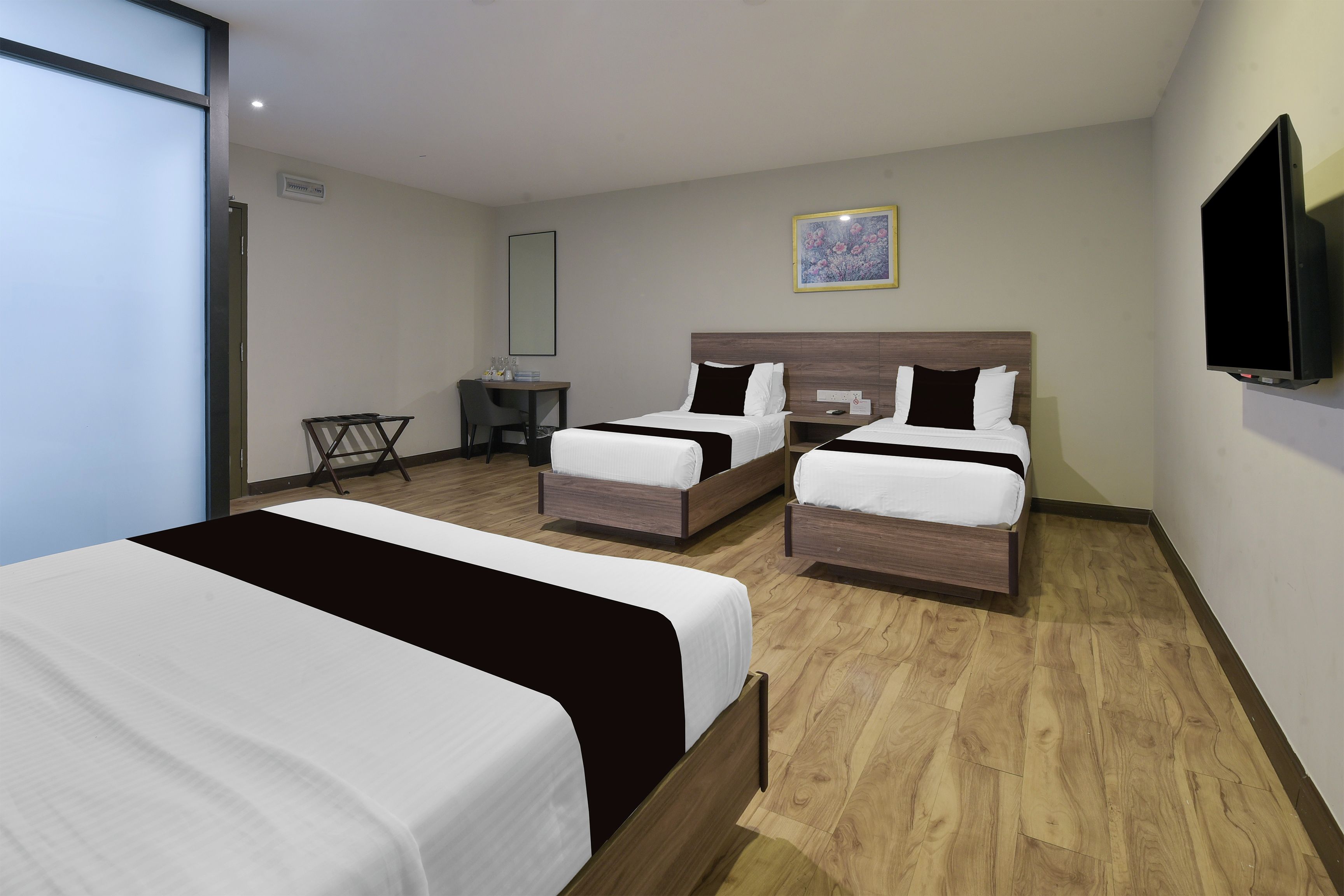 A hotel room with two single beds, a desk, a chair, a flat-screen TV, and a painting on the wall.