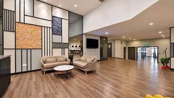 A spacious lobby with a wooden floor, two sofas, a small round table, and a colorful abstract painting on the wall.