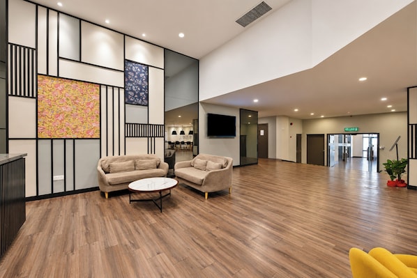 Un hall d’entrée spacieux avec un plancher en bois, deux canapés, une petite table ronde et un tableau abstrait aux couleurs vives accroché au mur.