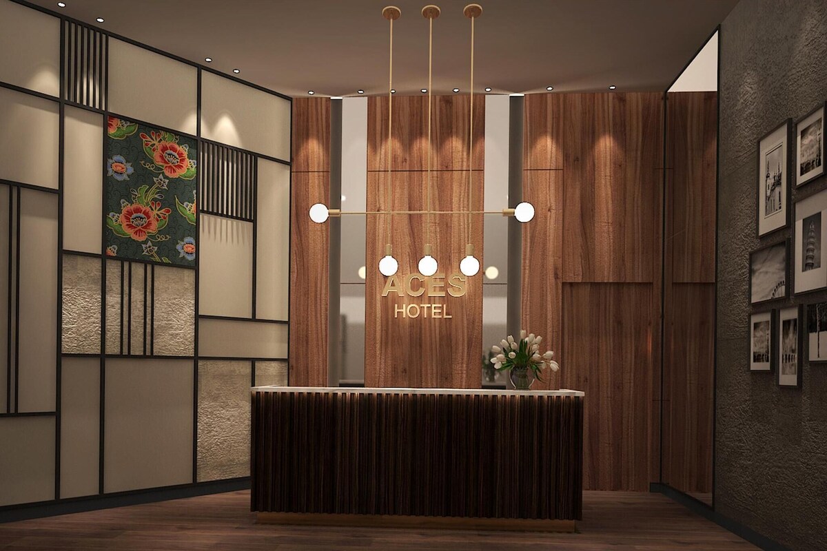 A reception desk with a wooden finish, a floral painting on the wall, and a sign reading 'ACES HOTEL.'