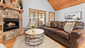 A cozy living room with a stone fireplace, leather sofa, and a round coffee table. - Rustic Stonebridge Cabin, near Silver Dollar City Pools>Golf>Lake>Nature (Branson West)