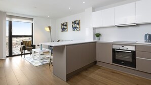 A modern kitchen with a built-in oven, a dining area with a table and chairs, and a large window offering a city view. - One Bedroom Lush Apartment Next to Wembley Stadium (Wembley Park)