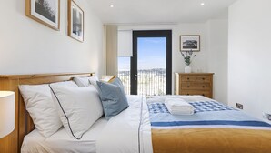 A hotel room with a bed, a dresser, a nightstand, a lamp, and a window with a view. - One Bedroom Lush Apartment Next to Wembley Stadium (Wembley Park)