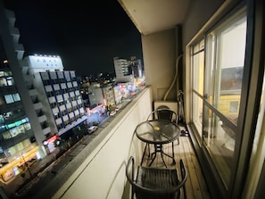 Uma varanda com mesa e cadeiras, com vista para um horizonte urbano iluminado à noite e uma visão clara do ambiente citadino.