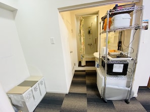 Quarto de hotel com cozinha compacta, chuveiro e pequeno espaço para guardar pertences.