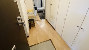 En smal hall med trägolv, en svart pall, en vit garderob och en säng med ett svart- och vitrutigt överkast i bakgrunden.